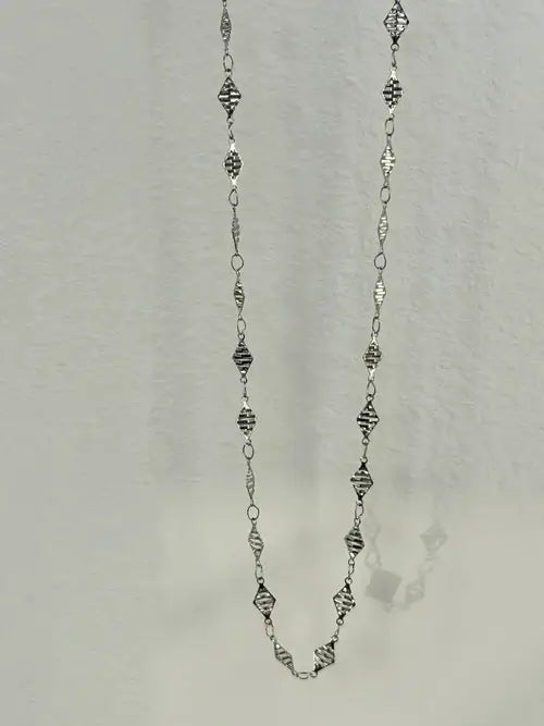 Long silver necklace with geometric patterned links, elegantly hanging against a light background.