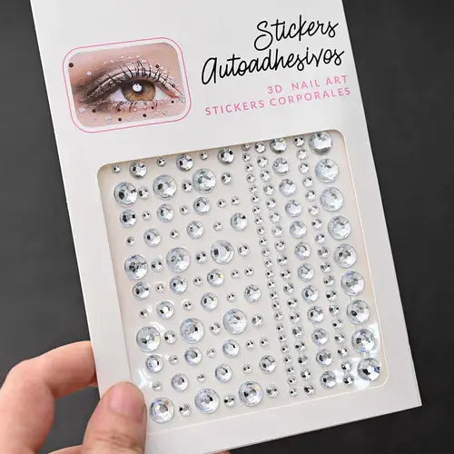 Hand holding a pack of iridescent face gem stickers for nail art featuring various shapes and sizes.
