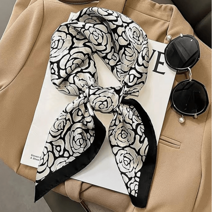 Vintage Luxe Satin Scarf with black and white rose pattern styled on a beige outfit with sunglasses and a magazine.
