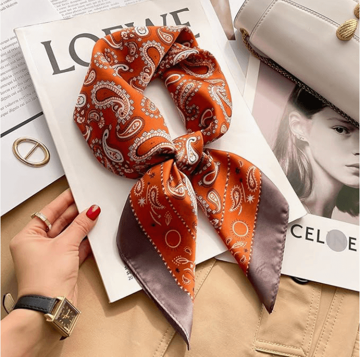 Vintage Luxe Satin Scarf in orange paisley design, styled as a bow on a magazine with gold accessories.